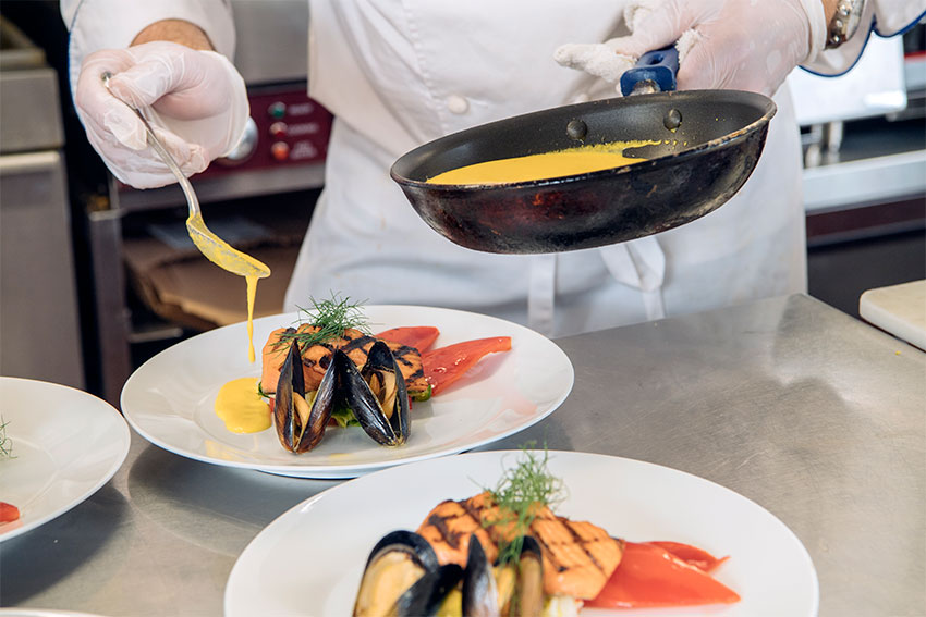 Adding sauce to a dinner of salmon and mussels